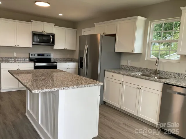 a kitchen with granite countertop a stove a sink a microwave a refrigerator and cabinets