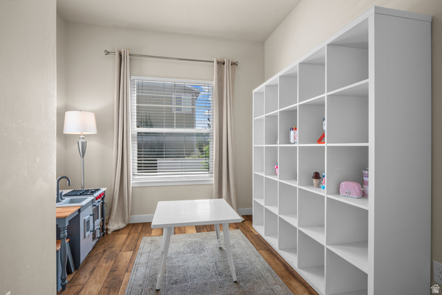 955 Delorean Lane Midvale, UT 84047 - Photo 16 of 47 Spacious room featuring a large window with blinds and drapes, wood-finish flooring, a neutral color palette, and extensive built-in shelving providing ample storage