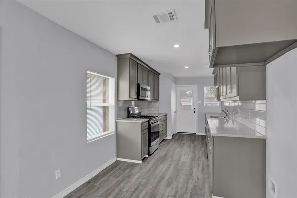 a kitchen with stainless steel appliances granite countertop a refrigerator oven a sink dishwasher and white cabinets with wooden floor