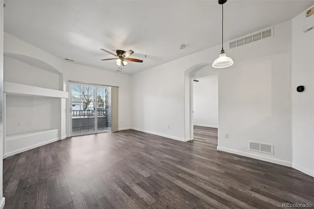 a view of an empty room with wooden floor and a ceiling fan