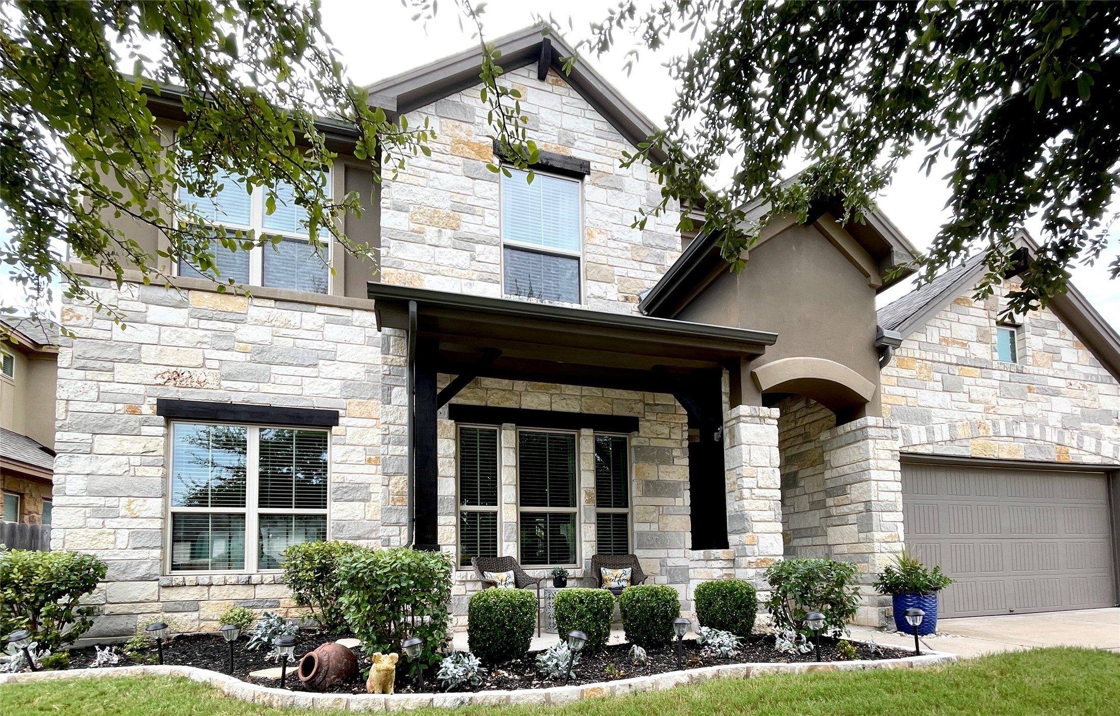 View of front of home with stone siding, covered porch, a garage, and driveway