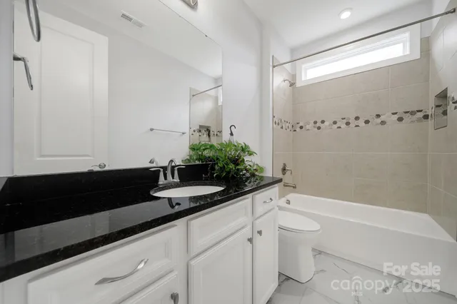 a bathroom with a granite countertop sink a toilet a mirror and bathtub