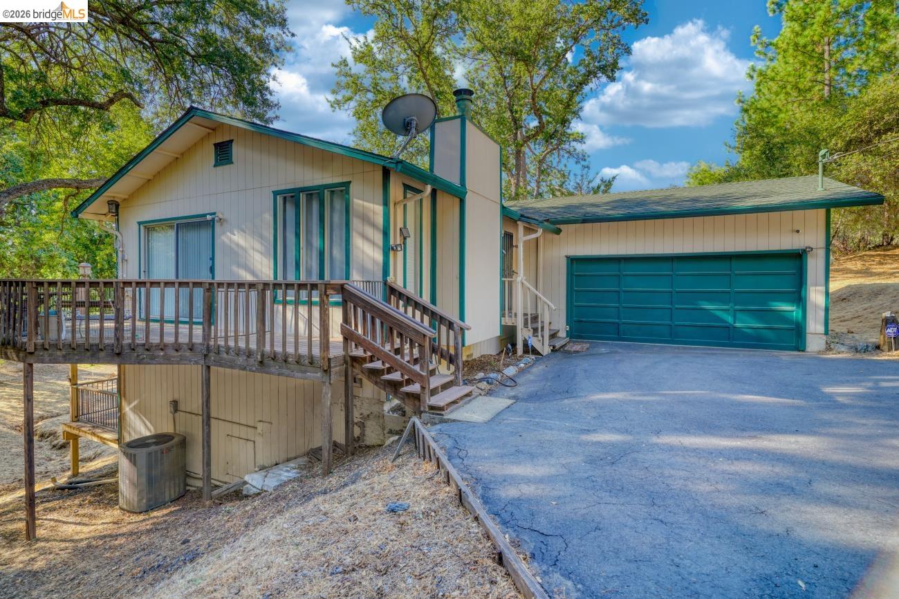 19215 Ferretti Road Groveland, CA 95321 - Photo 34 of 40 Exterior featuring a cream siding facade with green trim, an expansive wood deck, a wood staircase, a two-car garage with a green door, and a paved driveway