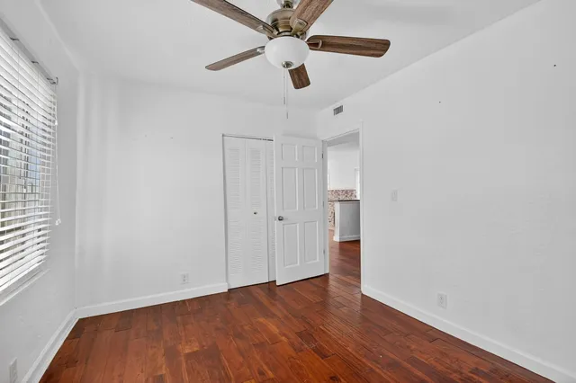 an empty room with wooden floor ceiling fan and window