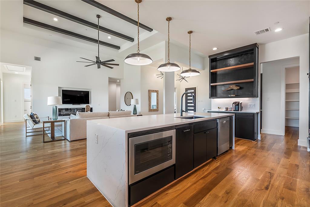 430 Whispering Way Red Oak, TX 75154 - Photo 21 of 40 Open-concept living space featuring a spacious kitchen island with integrated microwave, wood-finish flooring, vaulted ceilings with dark accent beams, a modern ceiling fan, and recessed shelving