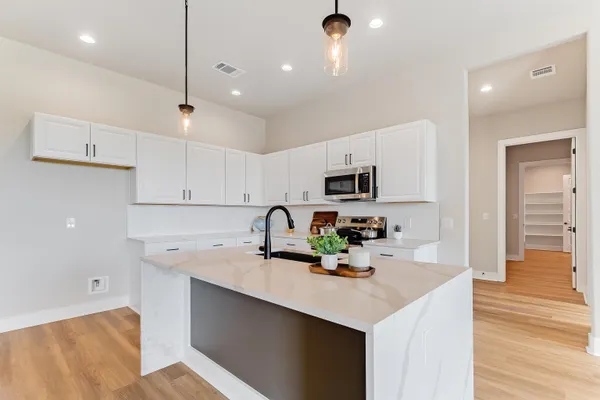 a kitchen with stainless steel appliances a sink a stove a refrigerator and white cabinets with wooden floor