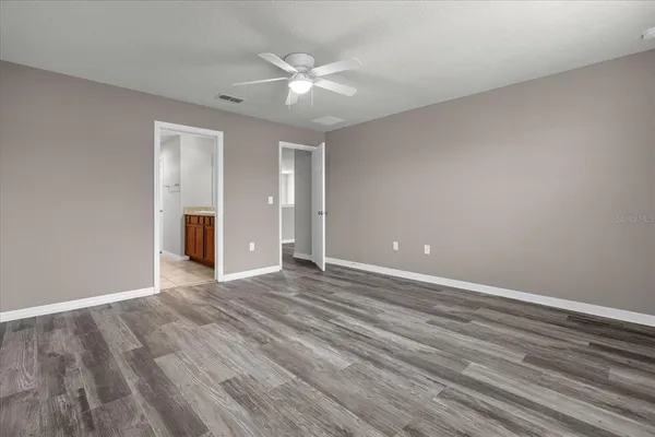 a view of an empty room with wooden floor and a ceiling fan