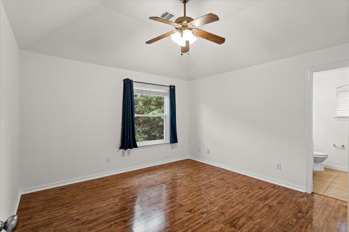 2304 Village View Loop Pflugerville, TX 78660 - Photo 39 of 40 A well-lit bedroom features vaulted ceilings, rich hardwood flooring, and a window with vibrant outdoor views.