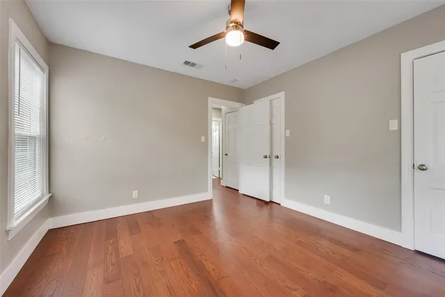 an empty room with wooden floor chandelier fan and windows