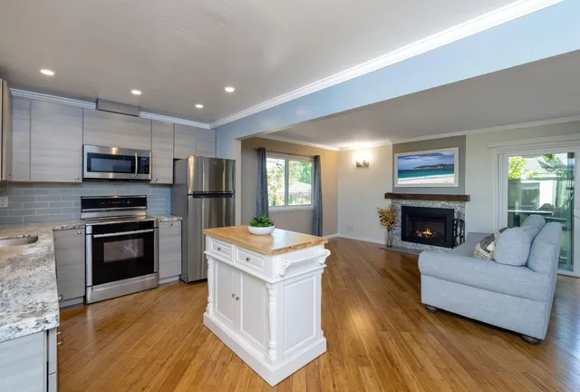 a living room with stainless steel appliances furniture a fireplace a flat screen tv and a fireplace