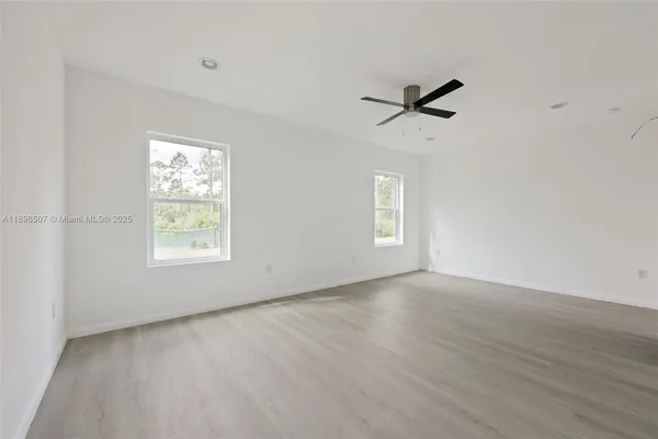 an empty room with wooden floor ceiling fan and windows