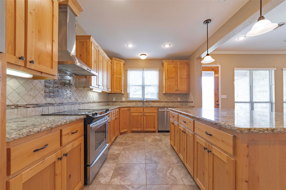 125 Walter Way Jarrell, TX 76537 - Photo 14 of 40 Kitchen featuring appliances with stainless steel finishes, wall chimney exhaust hood, decorative backsplash, light stone countertops, and recessed lighting
