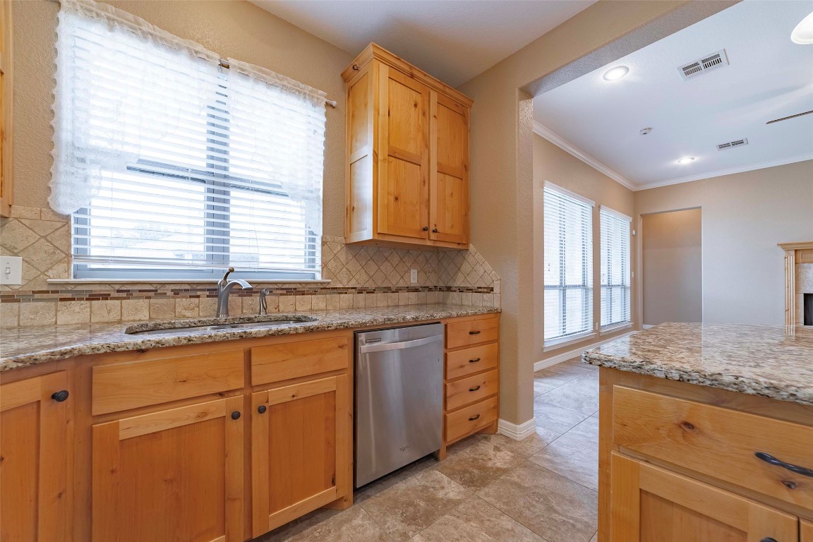 125 Walter Way Jarrell, TX 76537 - Photo 16 of 40 Kitchen with light stone counters, stainless steel dishwasher, tasteful backsplash, ornamental molding, and a fireplace