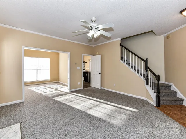 a view of an empty room with wooden floor and a chandelier fan
