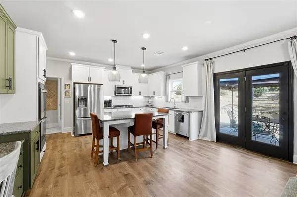 a kitchen with stainless steel appliances kitchen island granite countertop a refrigerator a stove a sink a dining table and chairs with wooden floor