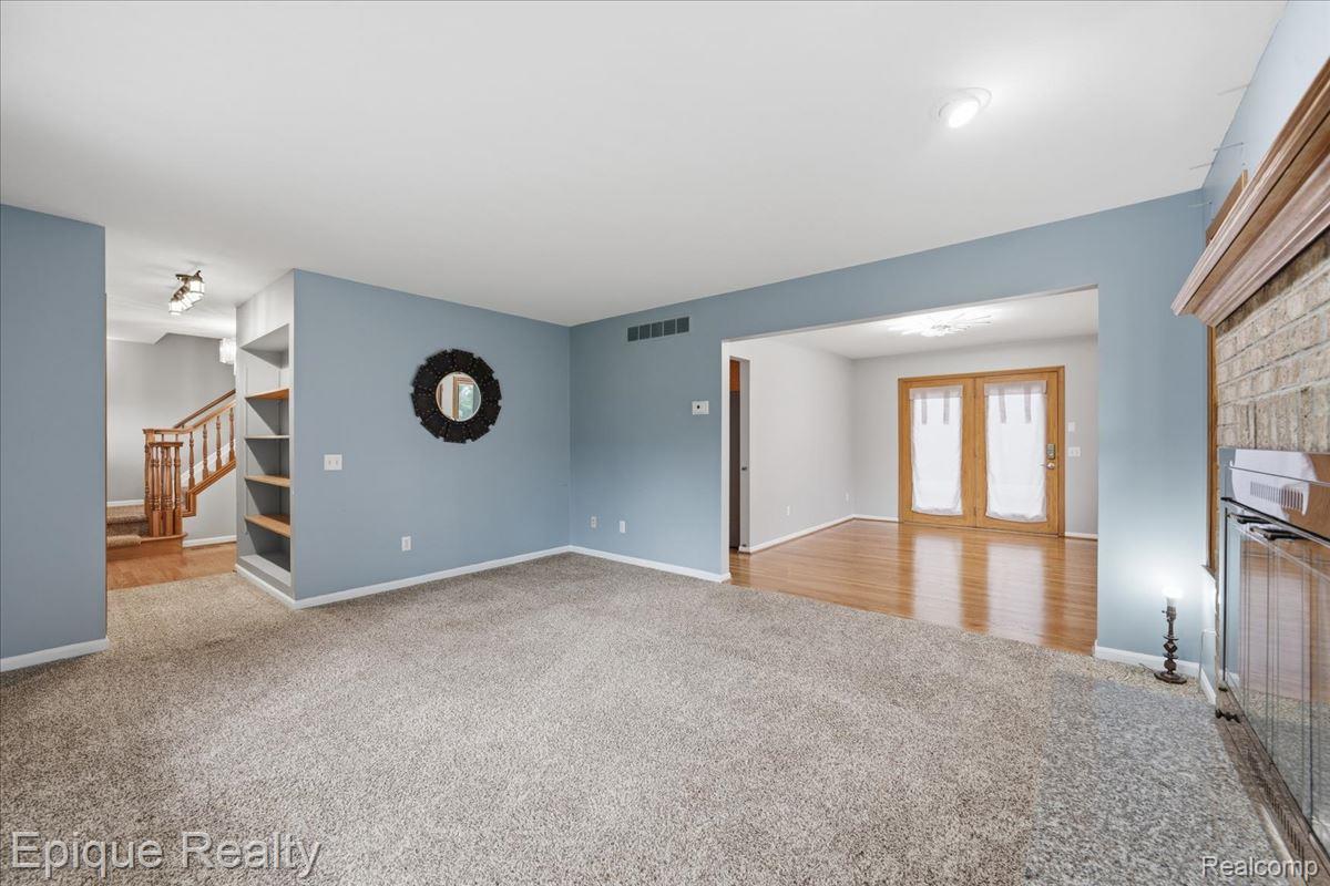 1221 Rhodes Road Lake Orion, MI 48360 - Photo 23 of 72 Spacious living area featuring light gray carpeting, a built-in shelving unit, and a fireplace with a brick surround