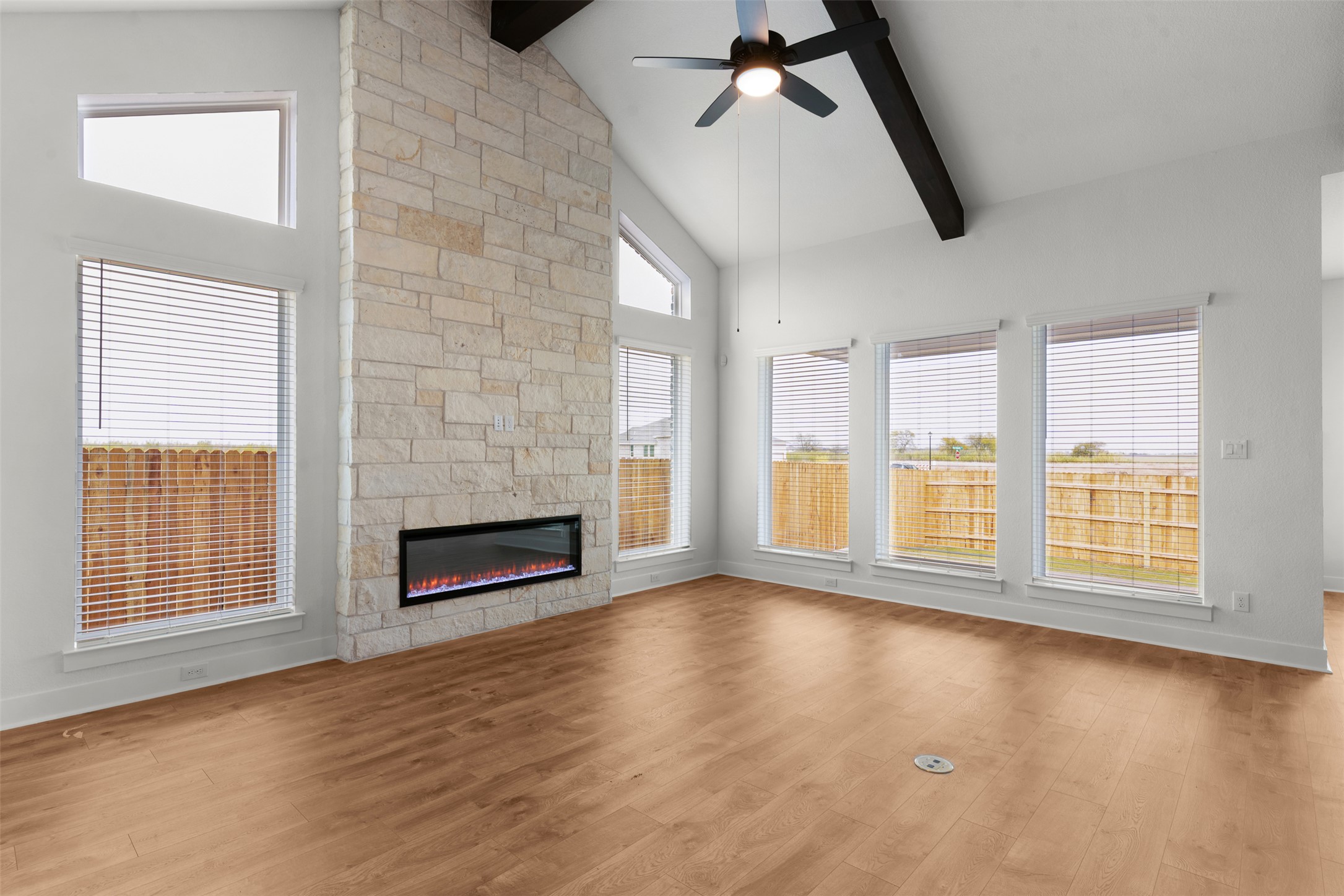 2312 Tobiano Trace Georgetown, TX 78633 - Photo 10 of 33 Spacious living area featuring a stone-clad fireplace with an electric insert, vaulted ceiling with exposed dark wood beam, ceiling fan, and wood-finish flooring