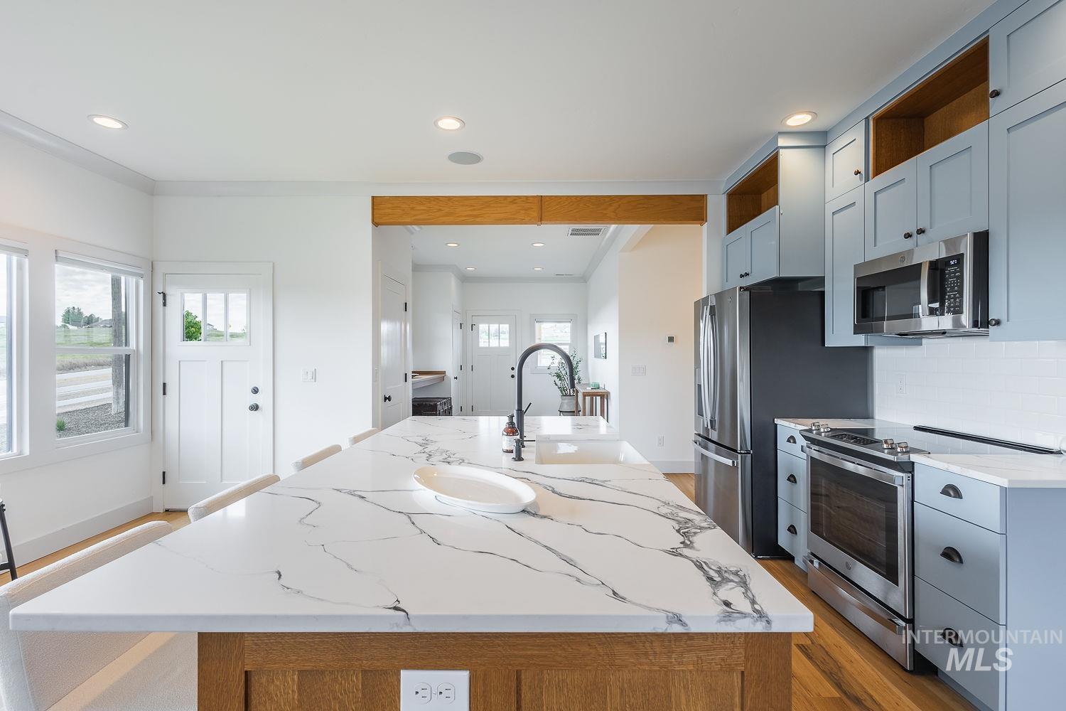 11171 Pump Road Nampa, ID 83686 - Photo 11 of 50 Spacious kitchen featuring an expansive island with a waterfall countertop, light blue cabinetry, stainless steel appliances, white subway tile backsplash, and wood-finish flooring