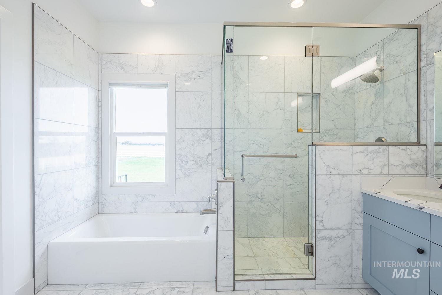 11171 Pump Road Nampa, ID 83686 - Photo 21 of 50 Bathroom featuring a built-in tub with a window, a glass-enclosed shower with a recessed niche, a vanity with a light blue cabinet, and a countertop with an integrated sink