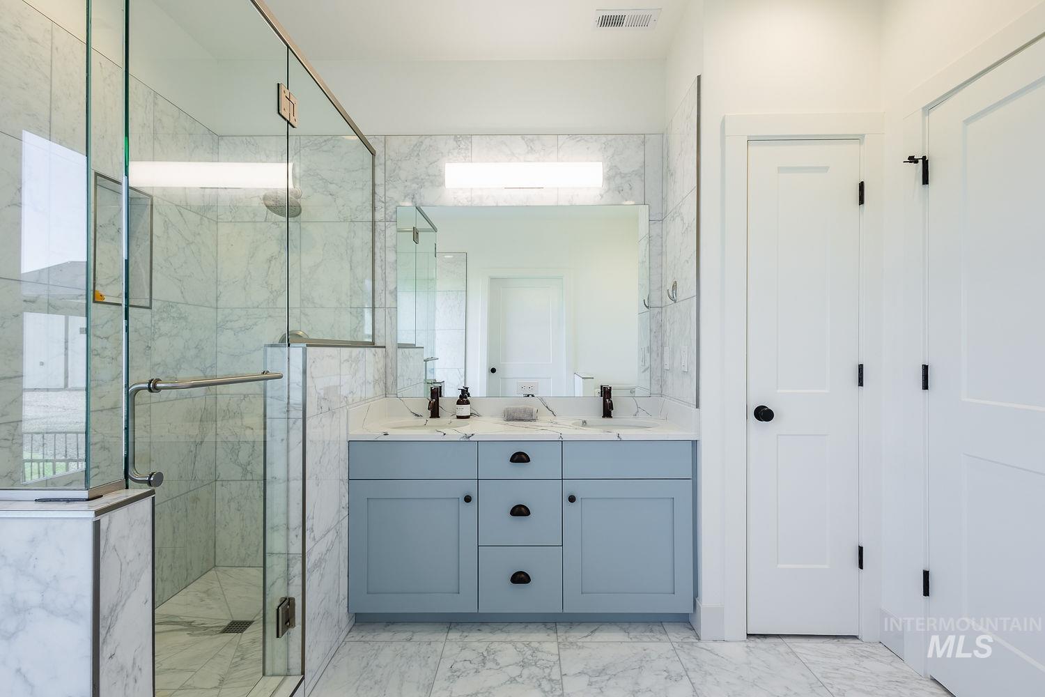 11171 Pump Road Nampa, ID 83686 - Photo 23 of 50 Spacious bathroom featuring a frameless glass shower enclosure, a double vanity with light blue cabinetry, and a large wall-mounted mirror