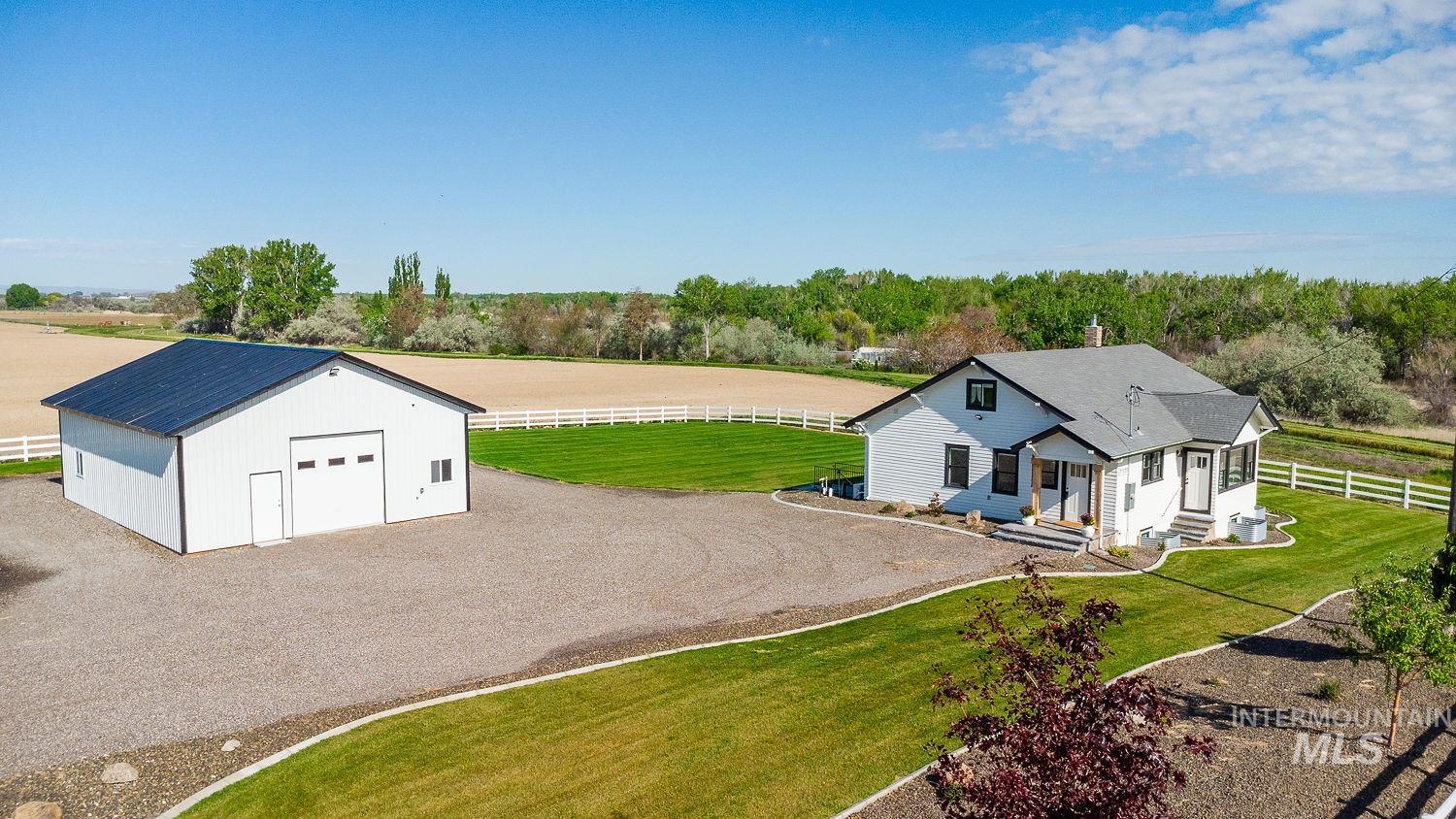 11171 Pump Road Nampa, ID 83686 - Photo 4 of 50 White modern farmhouse with a dark roof and trim, featuring a gravel driveway and surrounding green lawns
