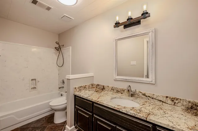 a bathroom with a granite countertop sink a toilet and shower