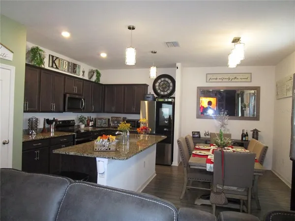 a kitchen with granite countertop a stove a sink a refrigerator and chairs