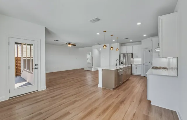 a view of an empty room with wooden floor and a kitchen