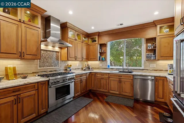 a kitchen with stainless steel appliances granite countertop wooden cabinets a sink dishwasher a stove and a refrigerator with wooden floor