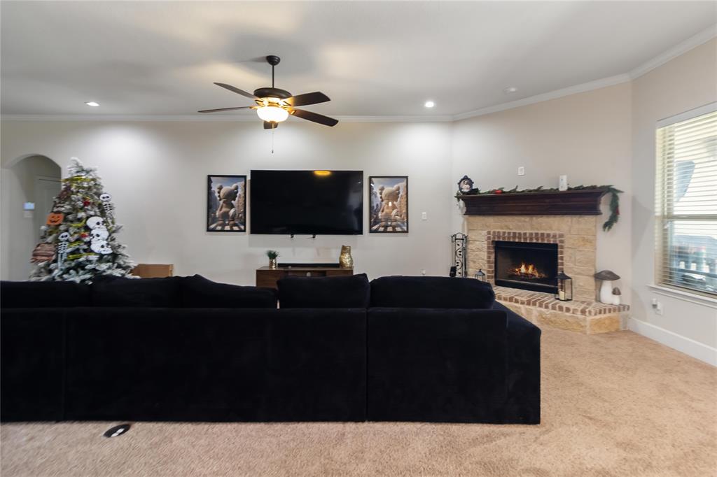 1663 Fraser Drive Burleson, TX 76028 - Photo 13 of 22 Carpeted living room with crown molding, a fireplace, ceiling fan, and recessed lighting