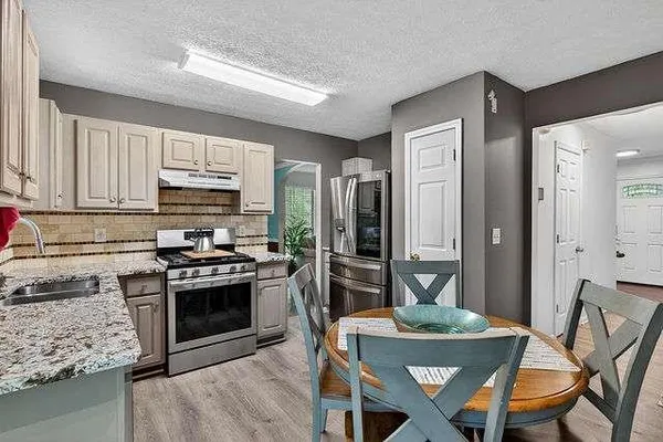 a kitchen with stainless steel appliances granite countertop a stove a sink dishwasher a refrigerator and a dining table with wooden floor