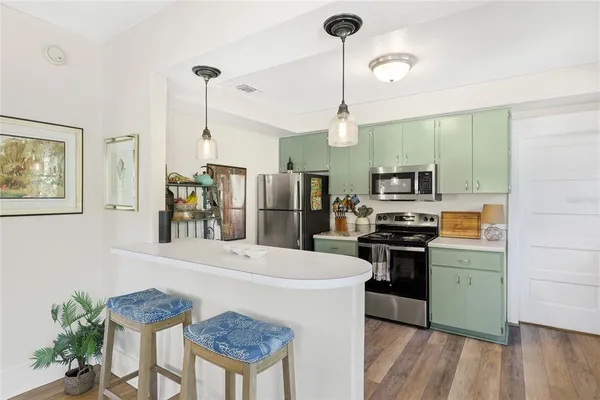 a kitchen with stainless steel appliances a stove a refrigerator a sink a dining table and chairs with wooden floor