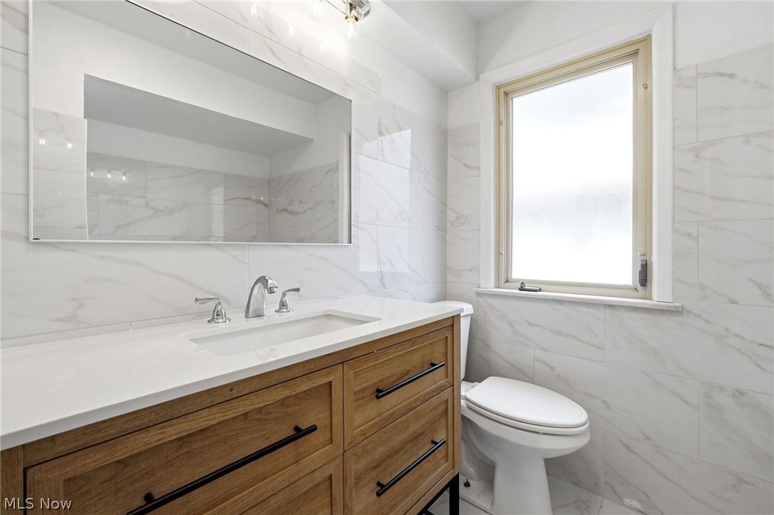2537 Edgewood Road Beachwood, OH 44122 - Photo 19 of 39 Bathroom featuring a wood-finish vanity with an integrated white sink, a wide rectangular mirror, chrome faucet fixtures, and white marble-look wall and floor tiling