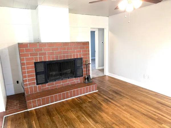 a view of an empty room with wooden floor and fireplace