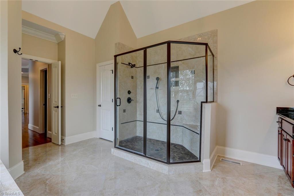 8501 Billet Place Oak Ridge, NC 27310 - Photo 13 of 30 Large walk in shower with decorative tile, 2 shower heads, and bench seating.