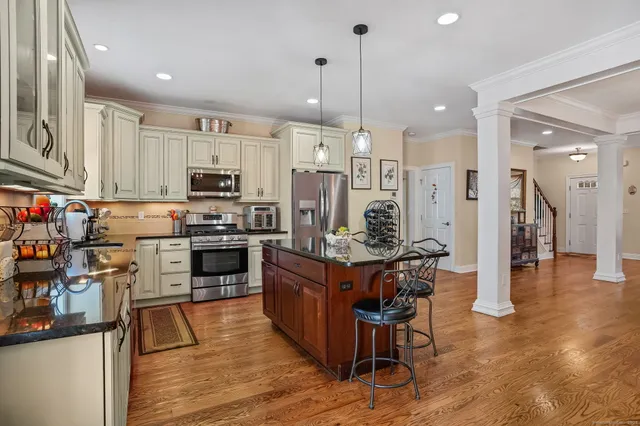 a kitchen with stainless steel appliances kitchen island granite countertop a refrigerator a stove top oven a sink dishwasher and a dining table with wooden floor