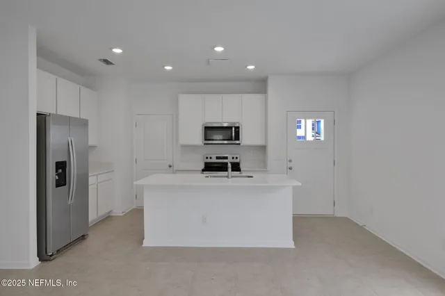 a view of kitchen with kitchen island stainless steel appliances a refrigerator and a stove top oven