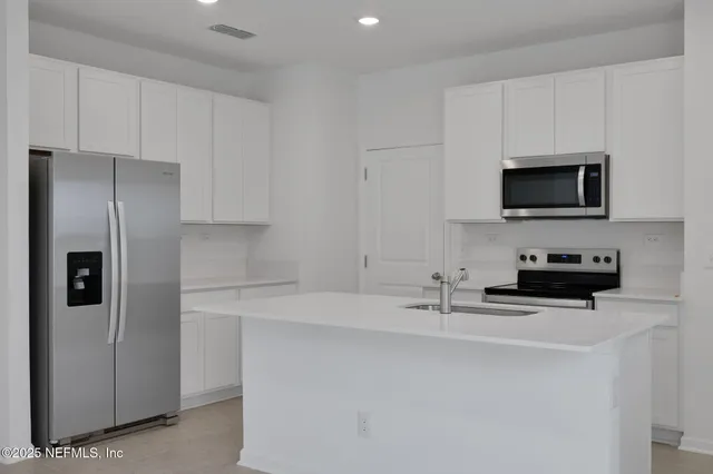 a kitchen with stainless steel appliances a refrigerator a stove a sink and a white cabinets