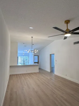 an empty room with wooden floor chandelier fan and windows