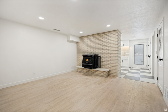 1168 East Center Street Bountiful, UT 84010 - Photo 30 of 38 Spacious room featuring light wood-finish flooring, recessed lighting, and a prominent brick-clad fireplace with a black stove insert