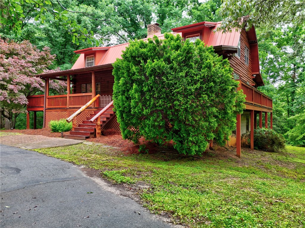 237 Spring Valley Road Liberty, SC 29657 - Photo 32 of 50 A rustic log cabin, nestled amidst lush trees, features a prominent red roof and an inviting porch with wooden stairs.