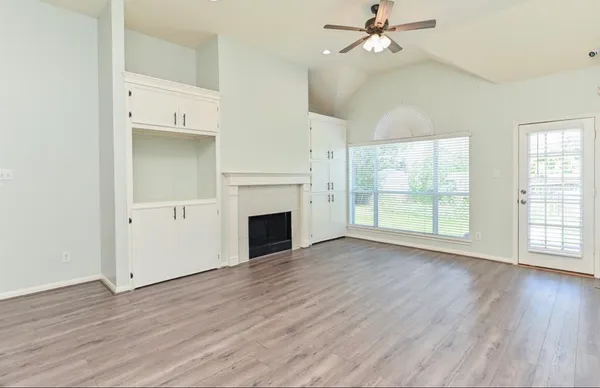 an empty room with wooden floor fireplace and windows