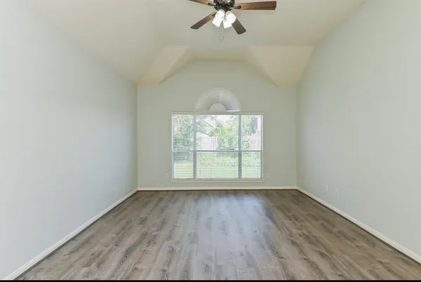 an empty room with wooden floor fan and windows