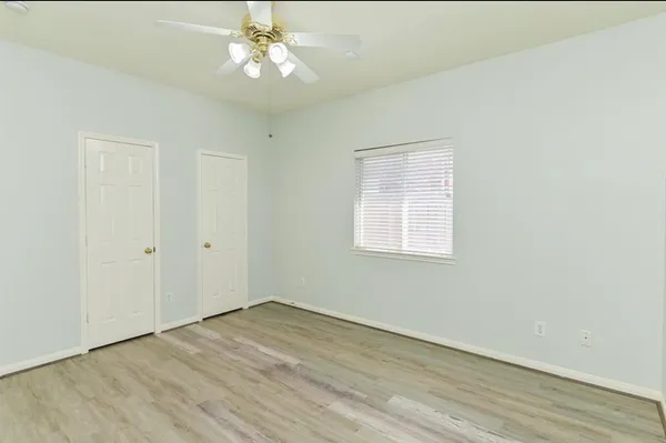 an empty room with wooden floor chandelier fan and windows