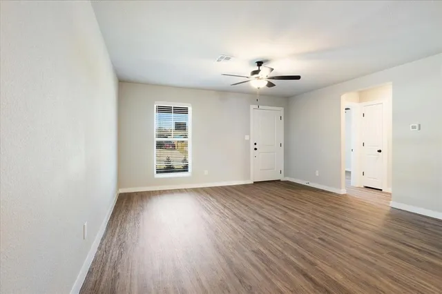 an empty room with wooden floor chandelier fan and windows