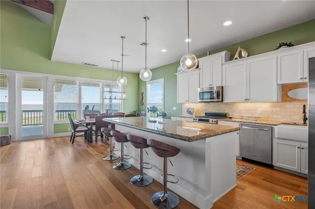 a kitchen with stainless steel appliances granite countertop a stove a sink a kitchen island with chairs and wooden floor