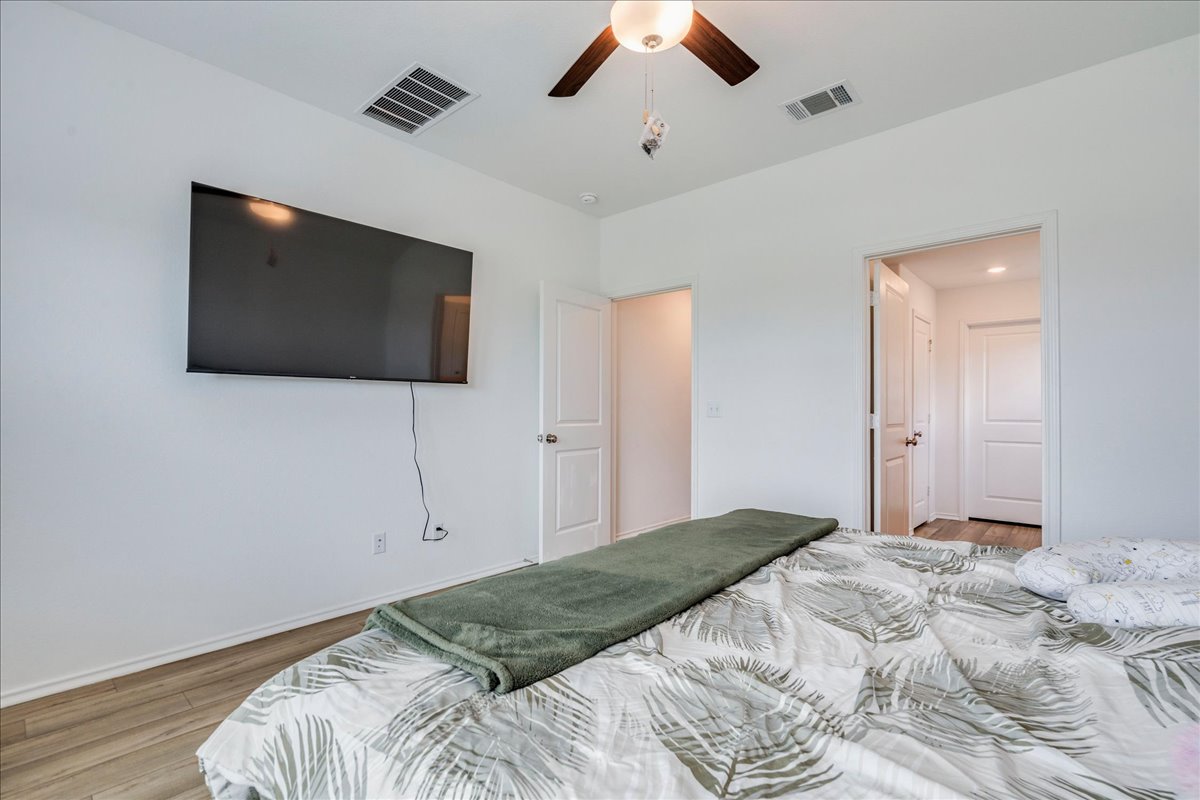 389 Salt Springs Road Kyle, TX 78640 - Photo 15 of 30 Relax in this tranquil bedroom, featuring light wood-look flooring and a functional ceiling fan for optimal comfort.