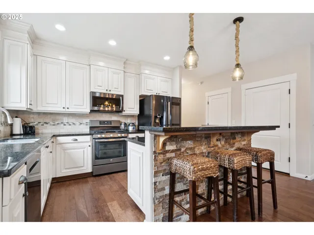 a kitchen with kitchen island granite countertop a stove a sink a oven a dining table and chairs with wooden floor