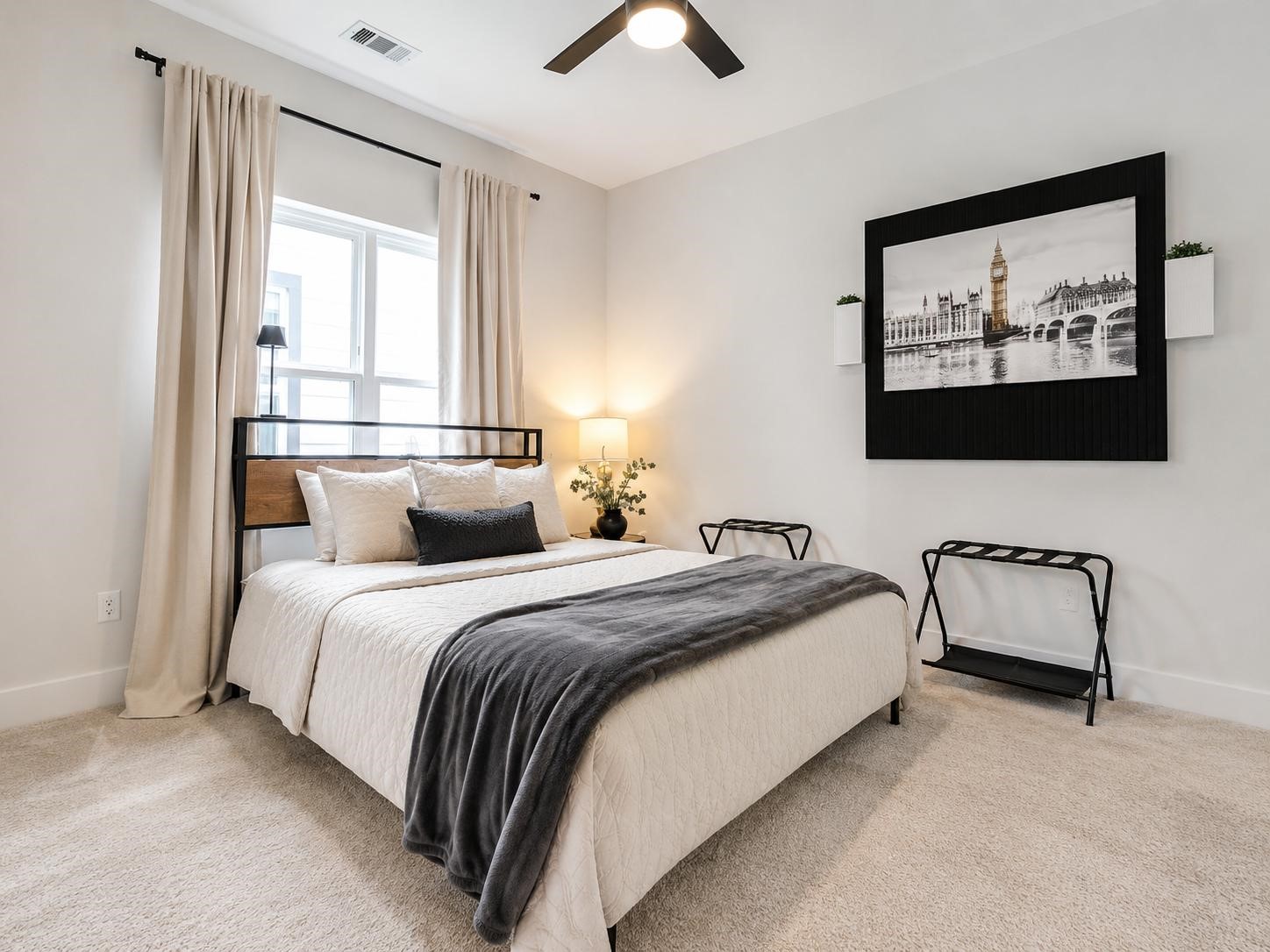 5407 Lee Street Houston, TX 77020 - Photo 8 of 17 This photo showcases a bright and modern bedroom with neutral tones. It features a cozy bed with soft bedding, a large window with elegant curtains, and a ceiling fan. A wall-mounted artwork adds a stylish touch, and the room has plush carpeting, creating a comfortable and inviting space.