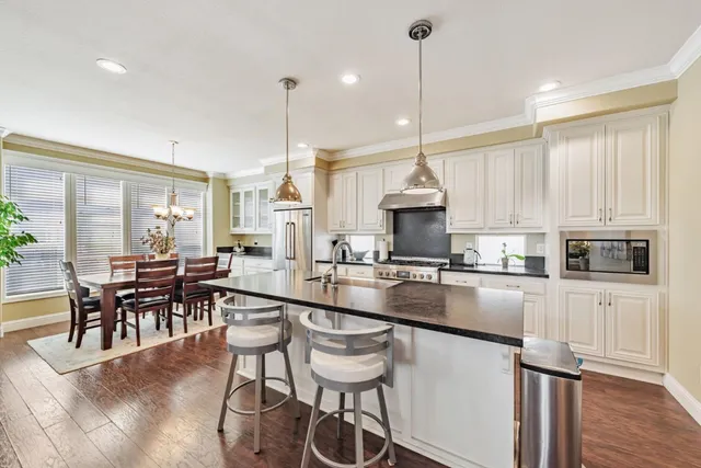 a kitchen with stainless steel appliances granite countertop a table chairs stove and white cabinets
